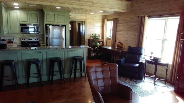 kitchen featuring a breakfast bar, stainless steel appliances, wooden walls, wooden ceiling, and dark stone countertops