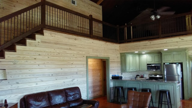 living room featuring high vaulted ceiling, ceiling fan, and wooden walls