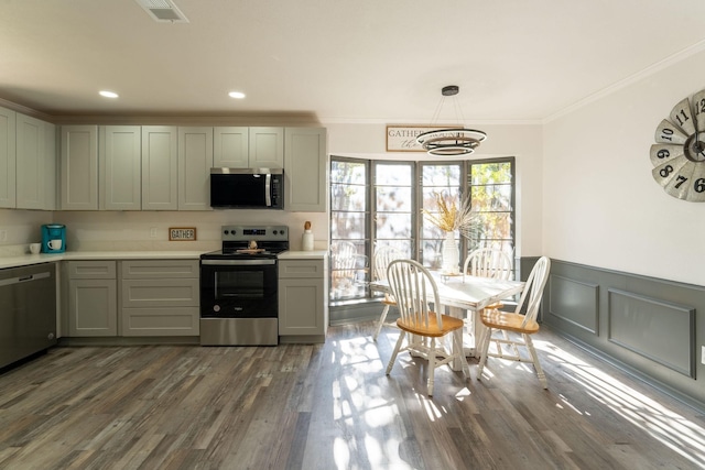 kitchen with crown molding, dark hardwood / wood-style flooring, hanging light fixtures, and appliances with stainless steel finishes