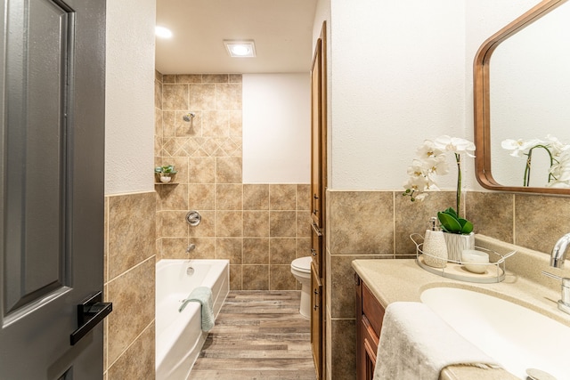 bathroom with a tub to relax in, tile walls, hardwood / wood-style floors, toilet, and vanity