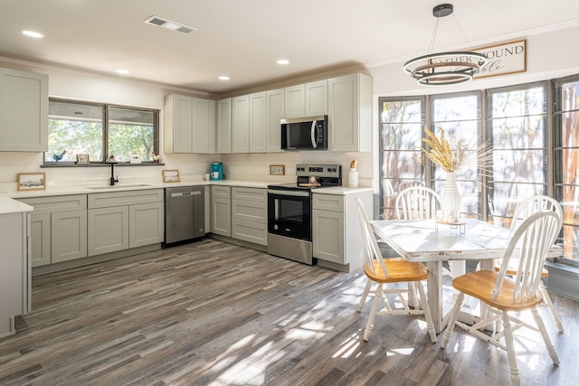 kitchen featuring hanging light fixtures, dark hardwood / wood-style flooring, sink, ornamental molding, and stainless steel appliances