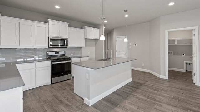 kitchen featuring white cabinets, decorative light fixtures, a kitchen island with sink, and appliances with stainless steel finishes