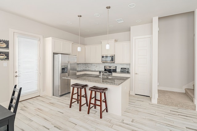 kitchen with a center island with sink, dark stone countertops, white cabinetry, and appliances with stainless steel finishes