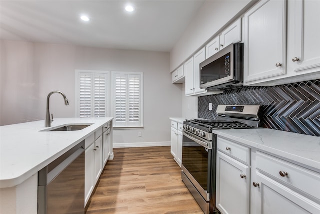 kitchen with decorative backsplash, light wood-type flooring, stainless steel appliances, sink, and white cabinets