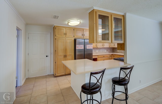 kitchen featuring a breakfast bar area, stainless steel refrigerator, kitchen peninsula, and light brown cabinetry