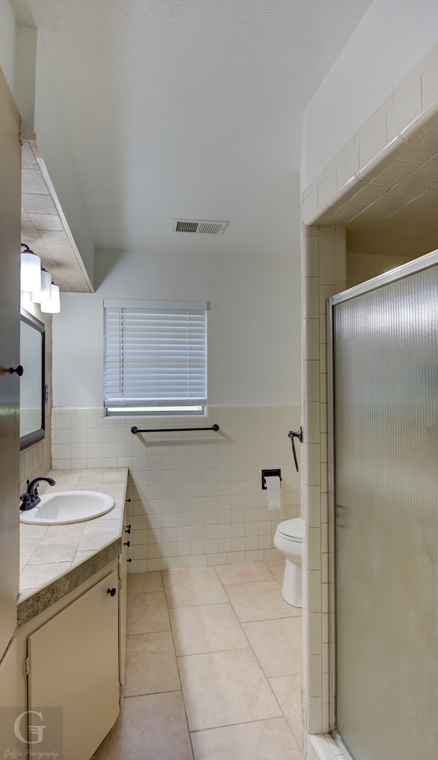 bathroom featuring tile patterned flooring, vanity, a shower with door, and tile walls