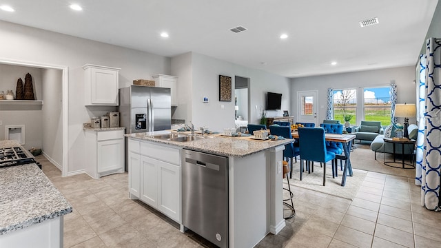 kitchen featuring a kitchen island with sink, sink, appliances with stainless steel finishes, light stone counters, and white cabinetry