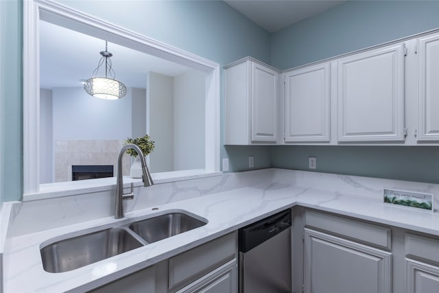 kitchen with light stone counters, sink, dishwasher, white cabinets, and hanging light fixtures