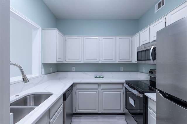 kitchen featuring light stone countertops, white cabinetry, sink, stainless steel appliances, and light hardwood / wood-style flooring