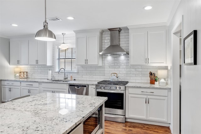 kitchen featuring white cabinets, wall chimney range hood, sink, decorative light fixtures, and stainless steel appliances