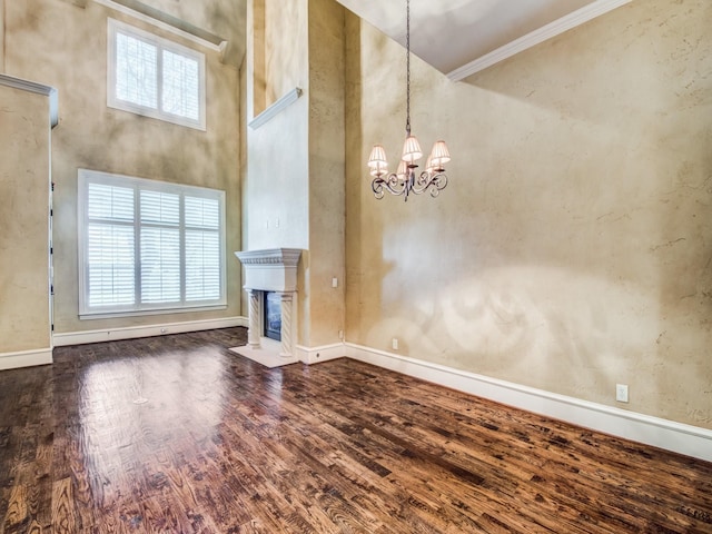 unfurnished living room with dark hardwood / wood-style flooring, a towering ceiling, a notable chandelier, and ornamental molding