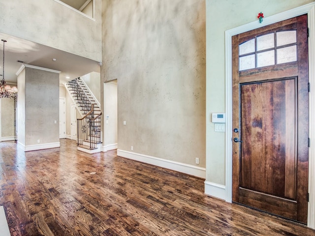 foyer featuring crown molding, a towering ceiling, dark hardwood / wood-style floors, and an inviting chandelier