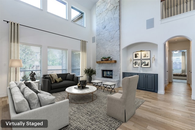 living room featuring a stone fireplace, light wood-type flooring, and a high ceiling