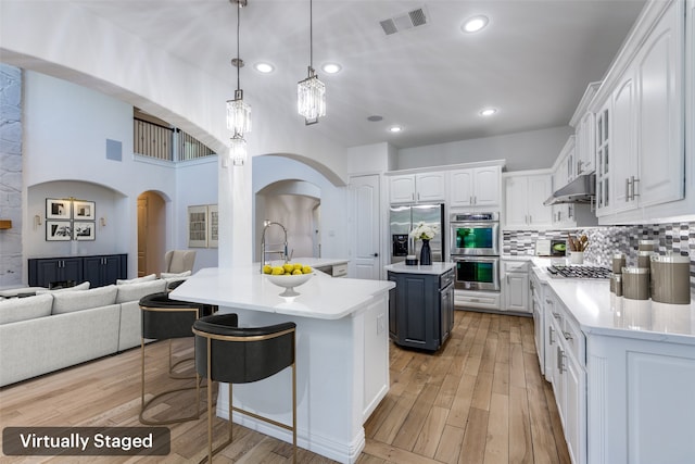 kitchen featuring appliances with stainless steel finishes, pendant lighting, a center island with sink, white cabinets, and light hardwood / wood-style floors