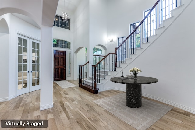 foyer entrance featuring hardwood / wood-style floors, a towering ceiling, an inviting chandelier, and french doors