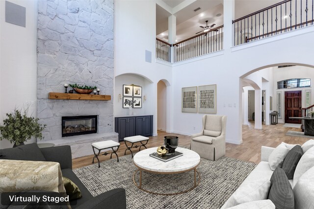 living room with ceiling fan, a fireplace, a high ceiling, and light hardwood / wood-style flooring