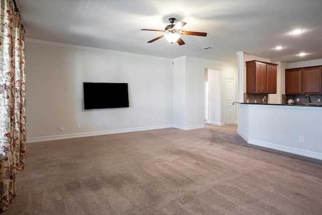 unfurnished living room featuring ornamental molding, sink, light colored carpet, and ceiling fan