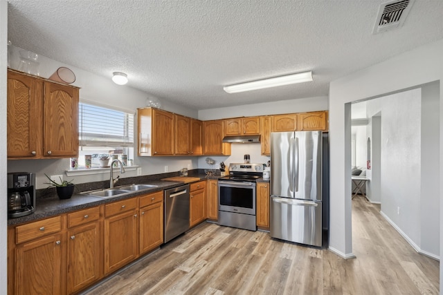 kitchen with appliances with stainless steel finishes, a textured ceiling, light hardwood / wood-style flooring, and sink