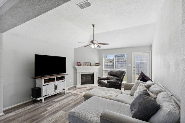 living room with hardwood / wood-style flooring, ceiling fan, a textured ceiling, and vaulted ceiling