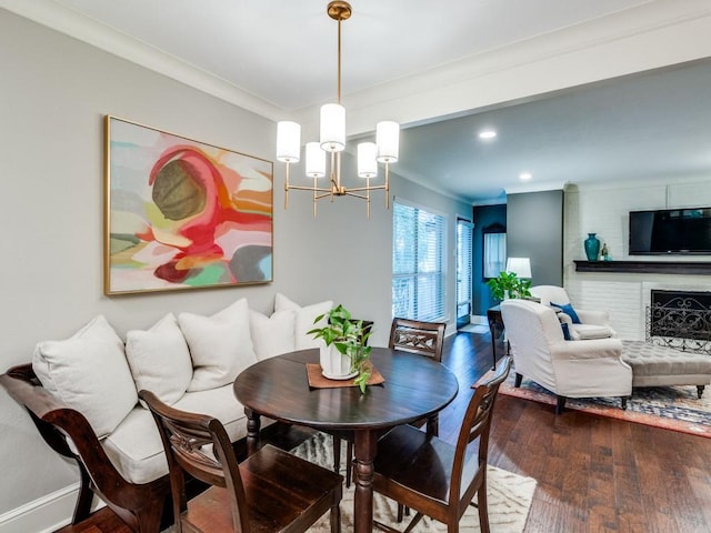 dining area featuring ornamental molding, a brick fireplace, dark wood-type flooring, and a notable chandelier