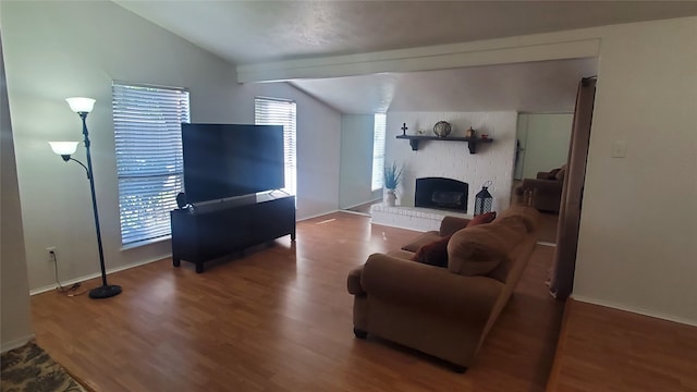 living room featuring vaulted ceiling with beams, hardwood / wood-style floors, and a brick fireplace