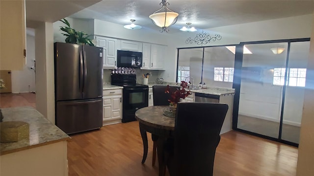 kitchen featuring pendant lighting, black appliances, light hardwood / wood-style flooring, light stone counters, and white cabinetry