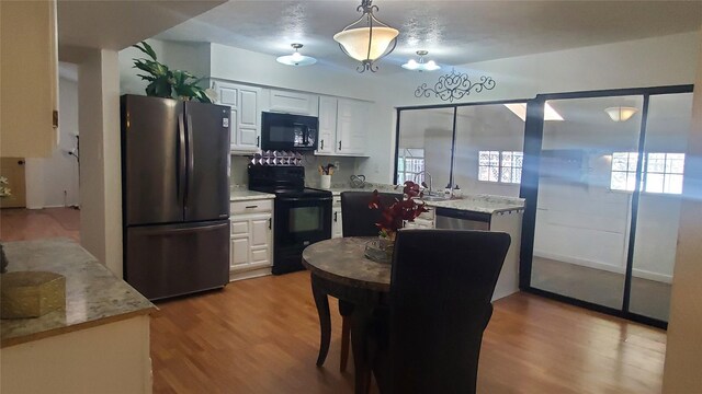 kitchen featuring pendant lighting, black appliances, light hardwood / wood-style flooring, light stone counters, and white cabinetry