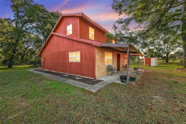 property exterior at dusk featuring a storage unit, a patio area, and a lawn