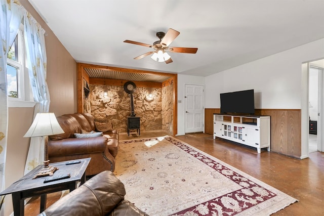 living room with a wood stove, ceiling fan, and wood walls