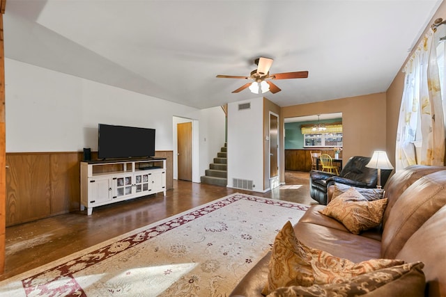 living room with ceiling fan with notable chandelier, dark hardwood / wood-style floors, and wooden walls