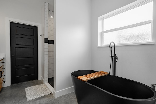 full bath with a freestanding tub, baseboards, a tile shower, and concrete flooring