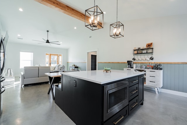 kitchen with concrete floors, beam ceiling, light countertops, stainless steel microwave, and dark cabinets