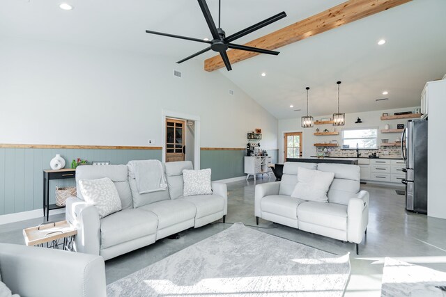 living area featuring beamed ceiling, high vaulted ceiling, concrete floors, and a wainscoted wall