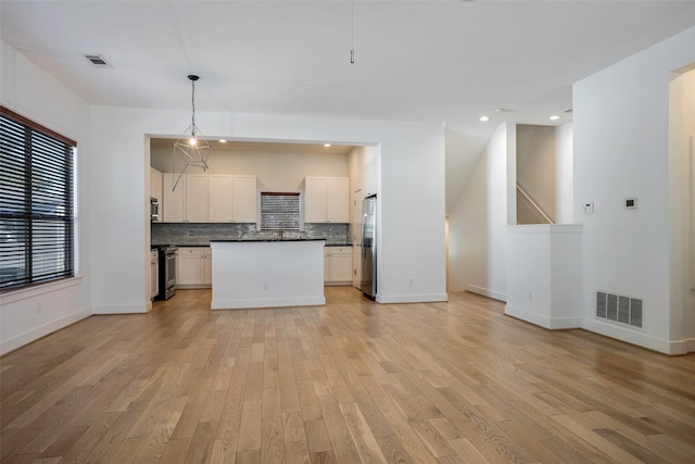 kitchen featuring white cabinets, backsplash, hanging light fixtures, stainless steel appliances, and light hardwood / wood-style flooring