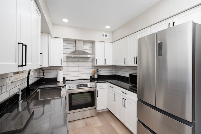 kitchen with white cabinets, wall chimney range hood, light hardwood / wood-style flooring, decorative backsplash, and stainless steel appliances