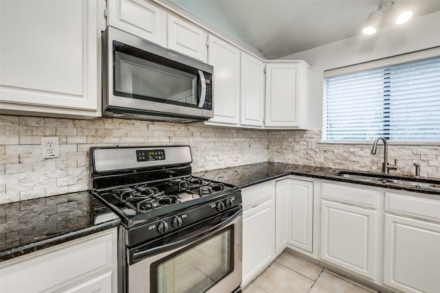 kitchen featuring stainless steel appliances, sink, white cabinets, light tile patterned flooring, and dark stone countertops