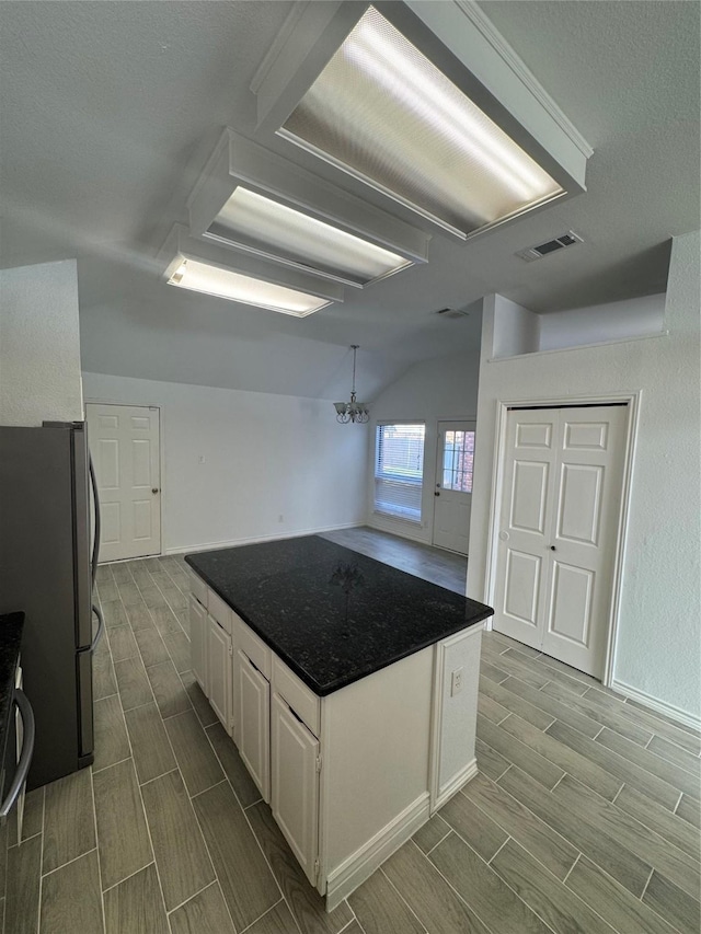 kitchen with vaulted ceiling, stainless steel refrigerator, a notable chandelier, a kitchen island, and white cabinetry