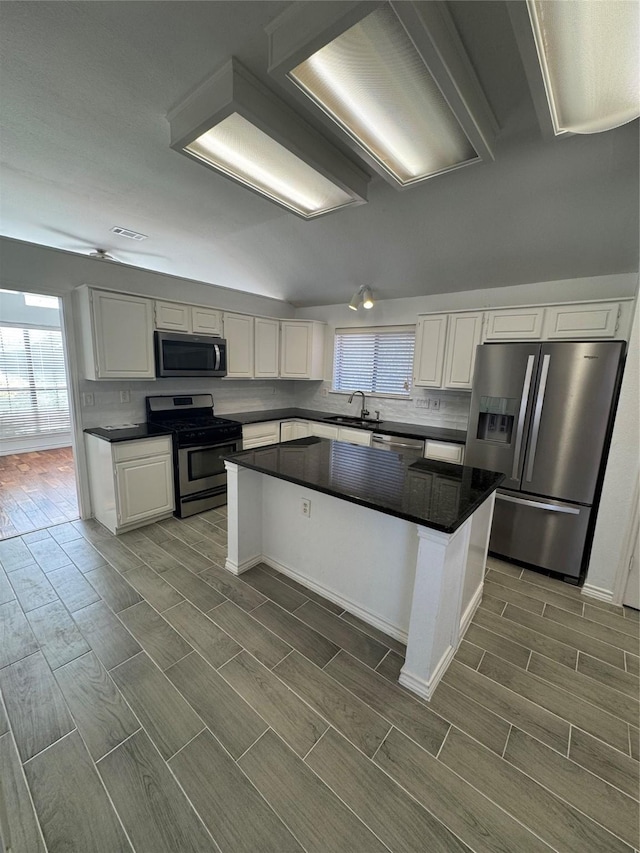 kitchen with stainless steel appliances, white cabinets, a center island, and tasteful backsplash