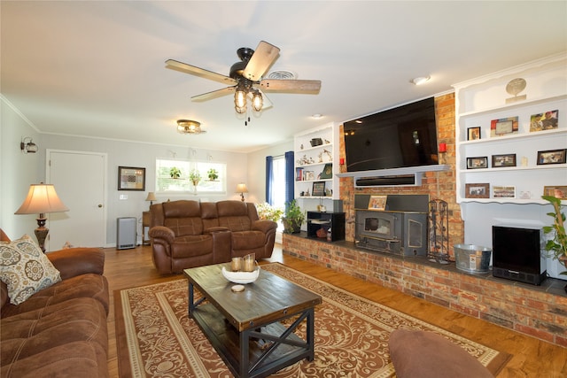 living room with a wood stove, ceiling fan, built in shelves, hardwood / wood-style flooring, and ornamental molding