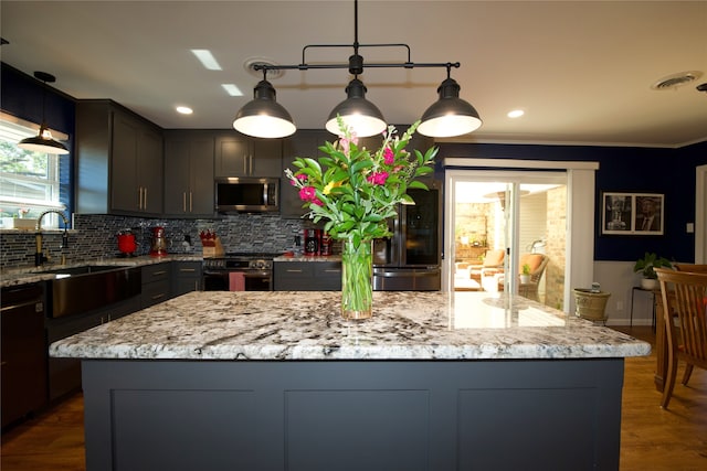 kitchen with light stone countertops, a kitchen island, pendant lighting, and appliances with stainless steel finishes