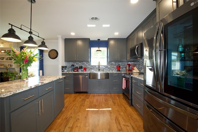 kitchen featuring sink, decorative backsplash, light wood-type flooring, appliances with stainless steel finishes, and decorative light fixtures