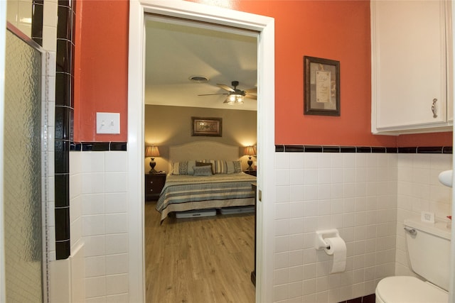 bedroom with light hardwood / wood-style flooring, ceiling fan, and tile walls