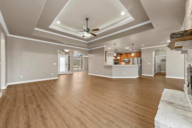 unfurnished living room with wood-type flooring, a tray ceiling, ceiling fan, and crown molding