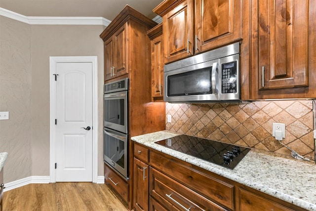 kitchen with tasteful backsplash, light stone counters, ornamental molding, stainless steel appliances, and light hardwood / wood-style floors