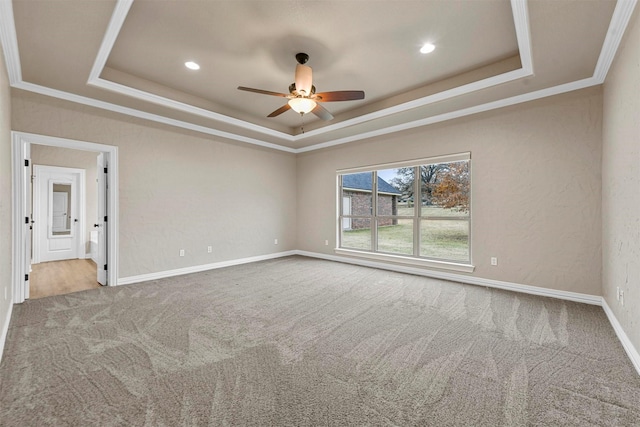 carpeted spare room with a raised ceiling, ceiling fan, and ornamental molding