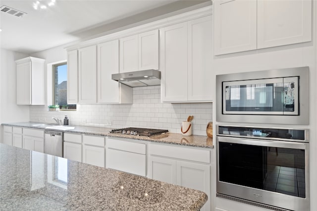 kitchen with white cabinets, light stone counters, backsplash, and appliances with stainless steel finishes