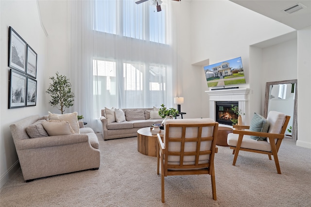 living room with ceiling fan, a towering ceiling, and light colored carpet