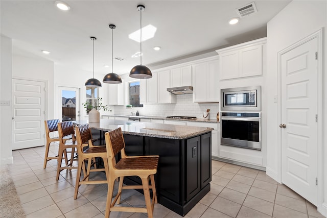 kitchen with white cabinetry, light stone countertops, hanging light fixtures, a kitchen island, and appliances with stainless steel finishes