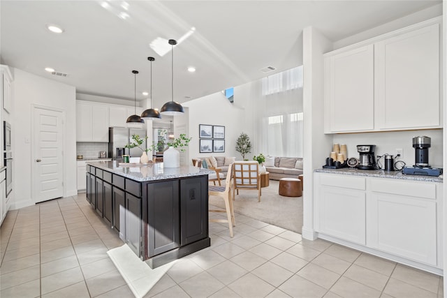 kitchen featuring a center island with sink, hanging light fixtures, stainless steel refrigerator with ice dispenser, light stone countertops, and white cabinetry