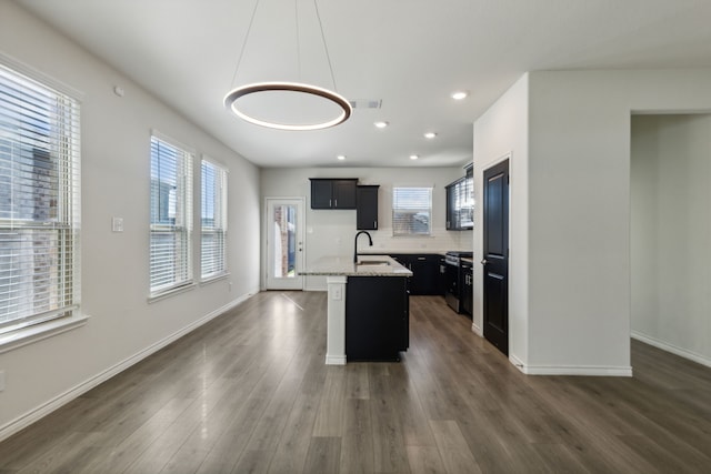 kitchen with a center island with sink, light stone counters, dark wood-type flooring, and a wealth of natural light